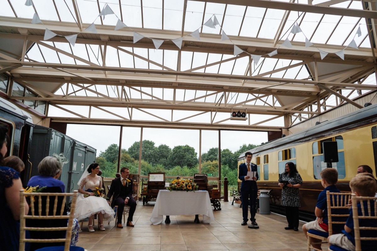 Liz and Paul’s wedding ceremony taking place between vintage trains at Buckinghamshire Railway Centre, with guests seated on either side.