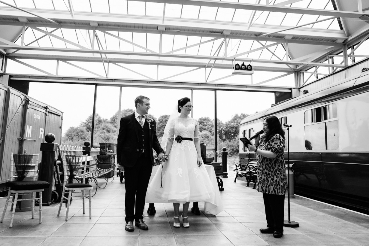 Bride and groom standing together beside a vintage train at Buckinghamshire Railway Centre.