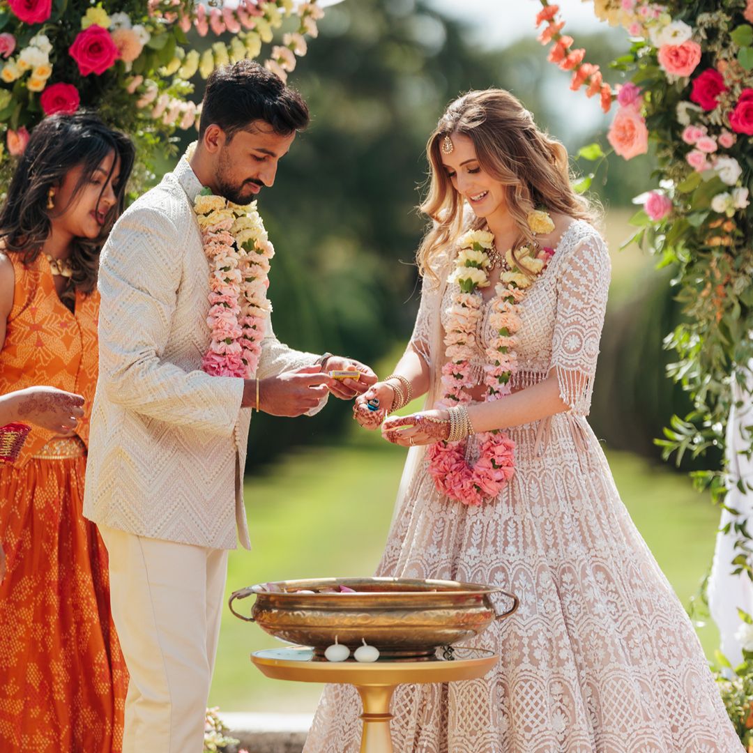 Natasha and Aaron take part in a traditional wedding ceremony outdoors, exchanging floral garlands beside a decorated ceremonial setup.