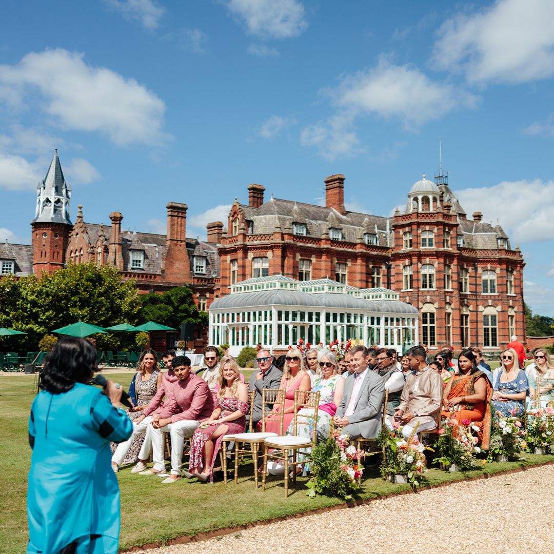 Guests gather on the lawn of a grand historic venue for Natasha and Aaron’s outdoor multicultural wedding ceremony.