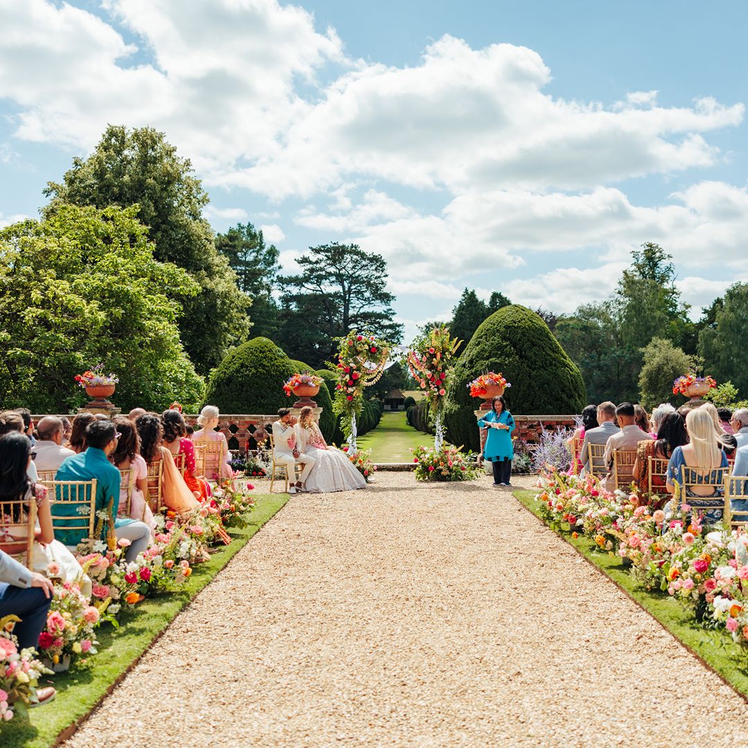 Guests are seated along a flower-lined aisle as Natasha and Aaron’s outdoor wedding ceremony takes place in a beautiful garden setting.