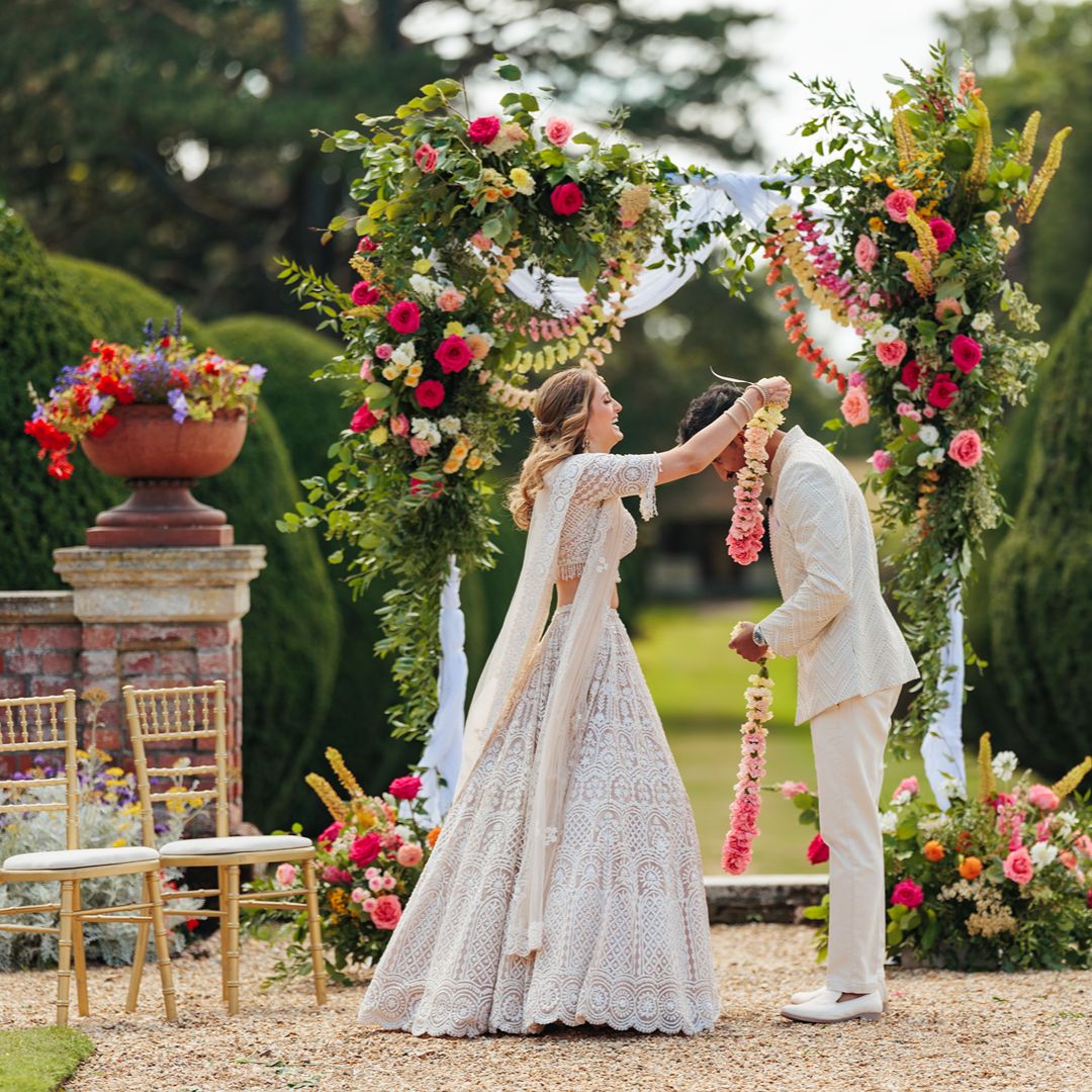 Natasha and Aaron exchange floral garlands beneath a beautifully decorated floral wedding arch during their outdoor ceremony.